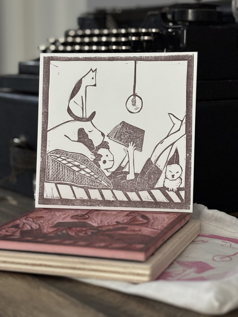 quadretto con una figura femminile stesa sul letto a leggere un libro circondata da un cane e un gatto